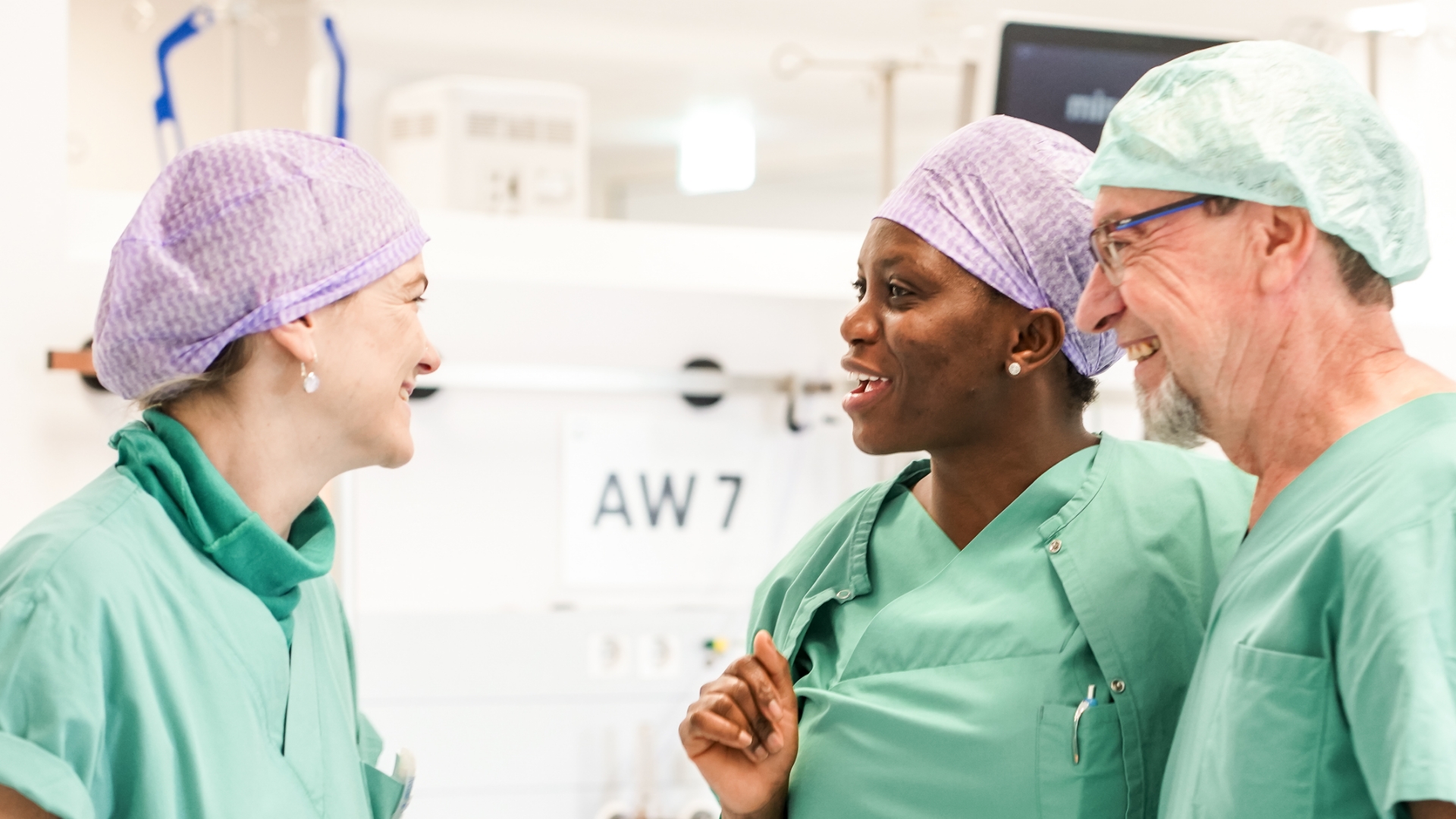 Zwei OP-Assistentinnen und ein Assisten im OP sich lachend unterhaltend 